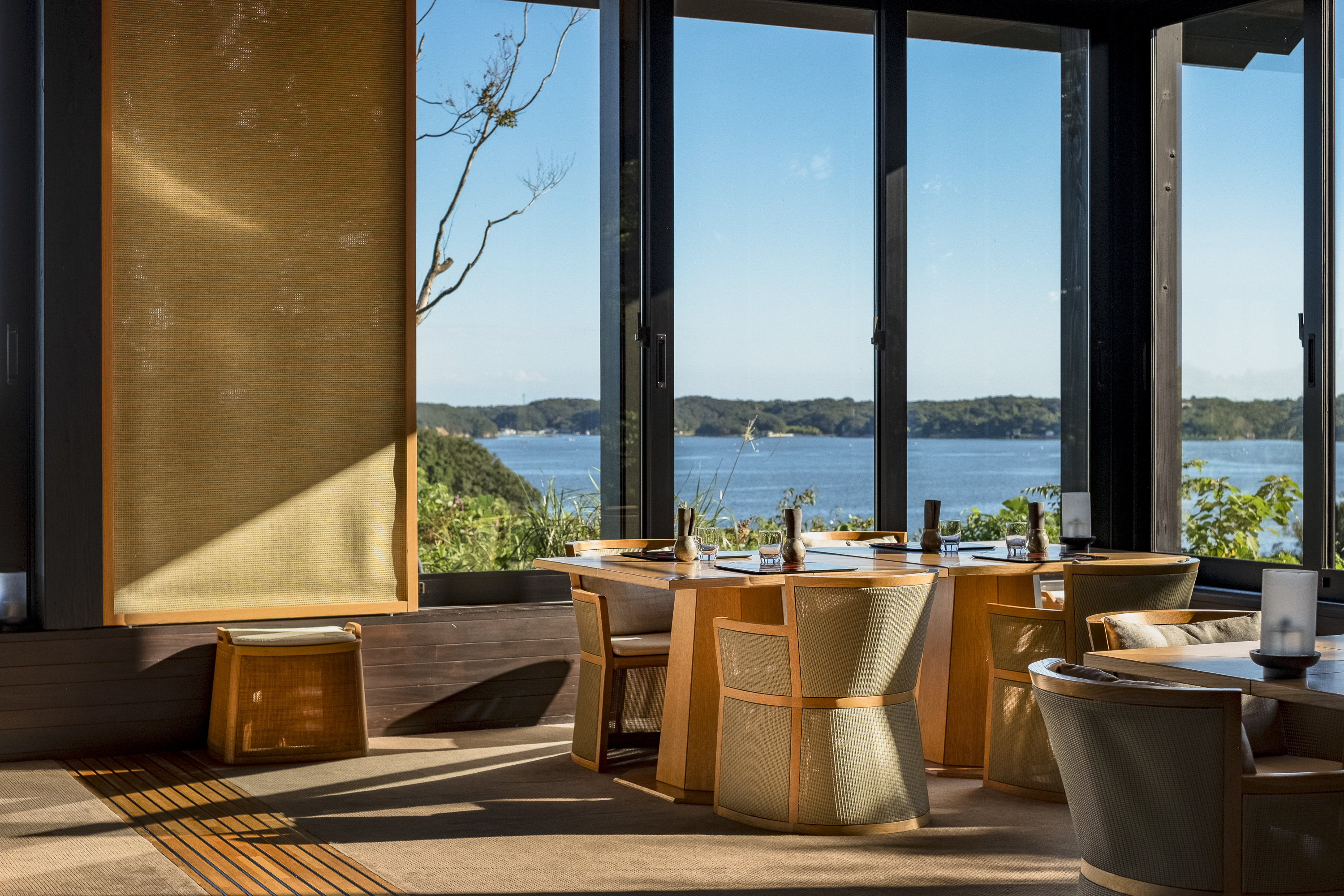 Dining tables set for a meal in a sunny window of the restaurant of Amanemu with a view of the ocean
