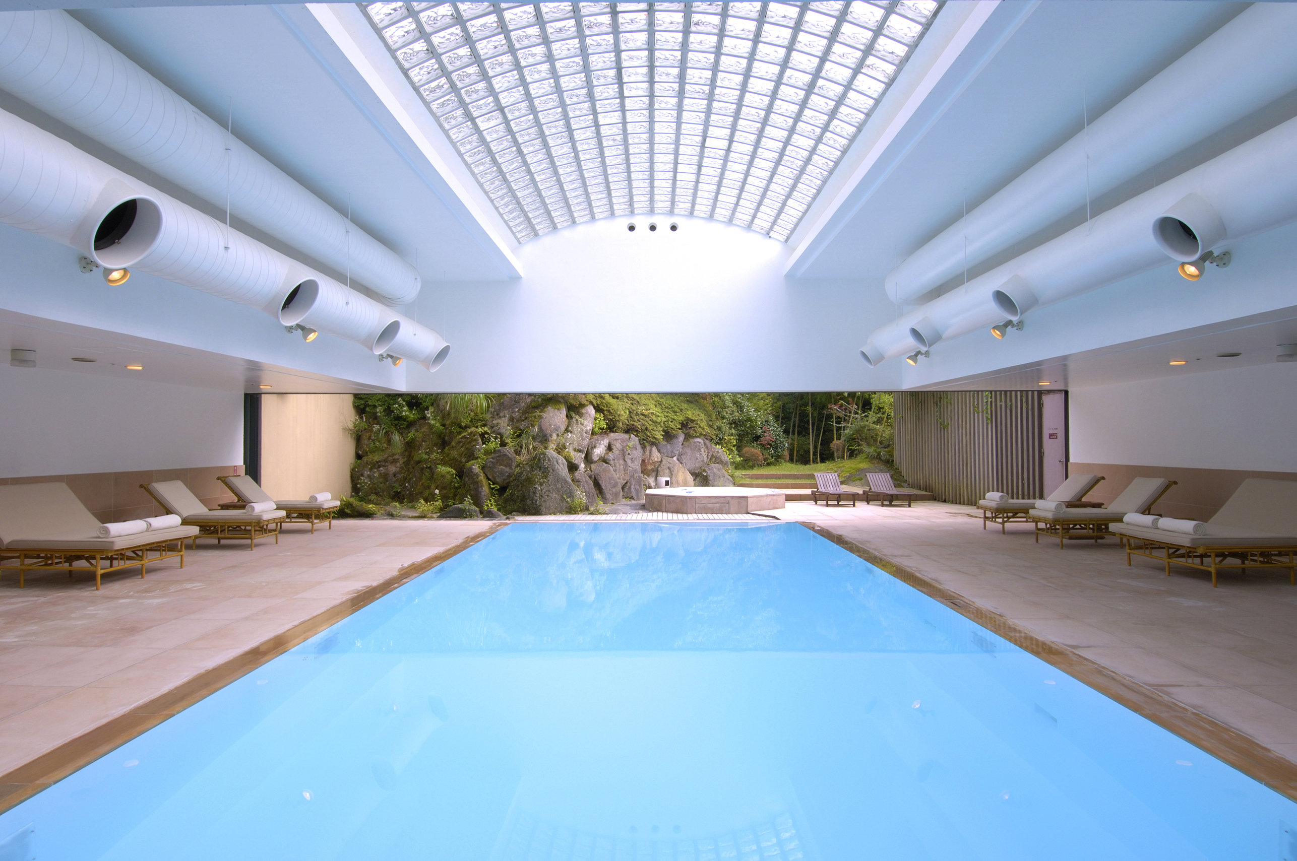 A sleek pool beneath a white arched roof with open walls looking out onto gardens