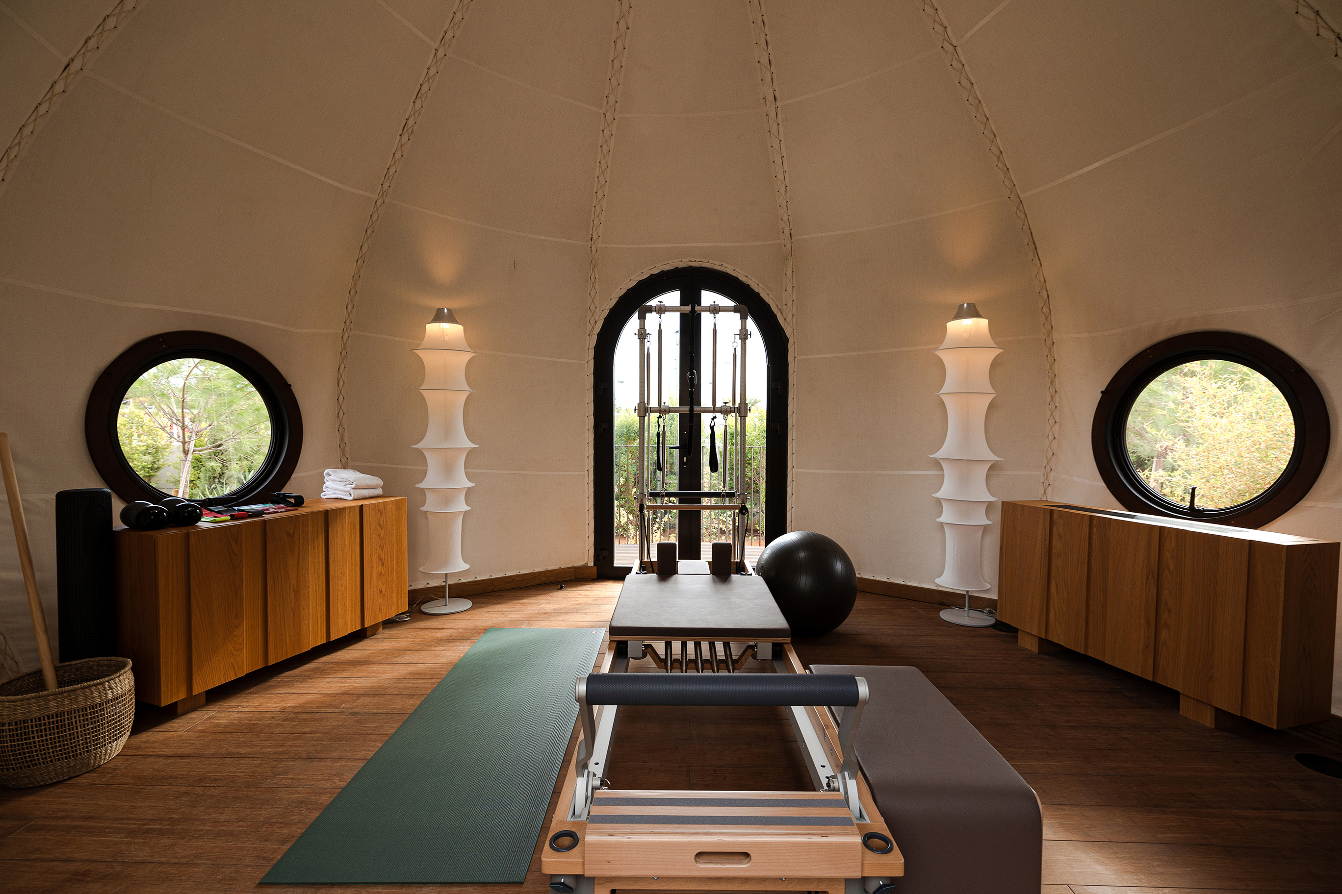 A tented yoga studio with a reformer Pilates bench, yoga mat, circular windows and sleek wooden furnishings