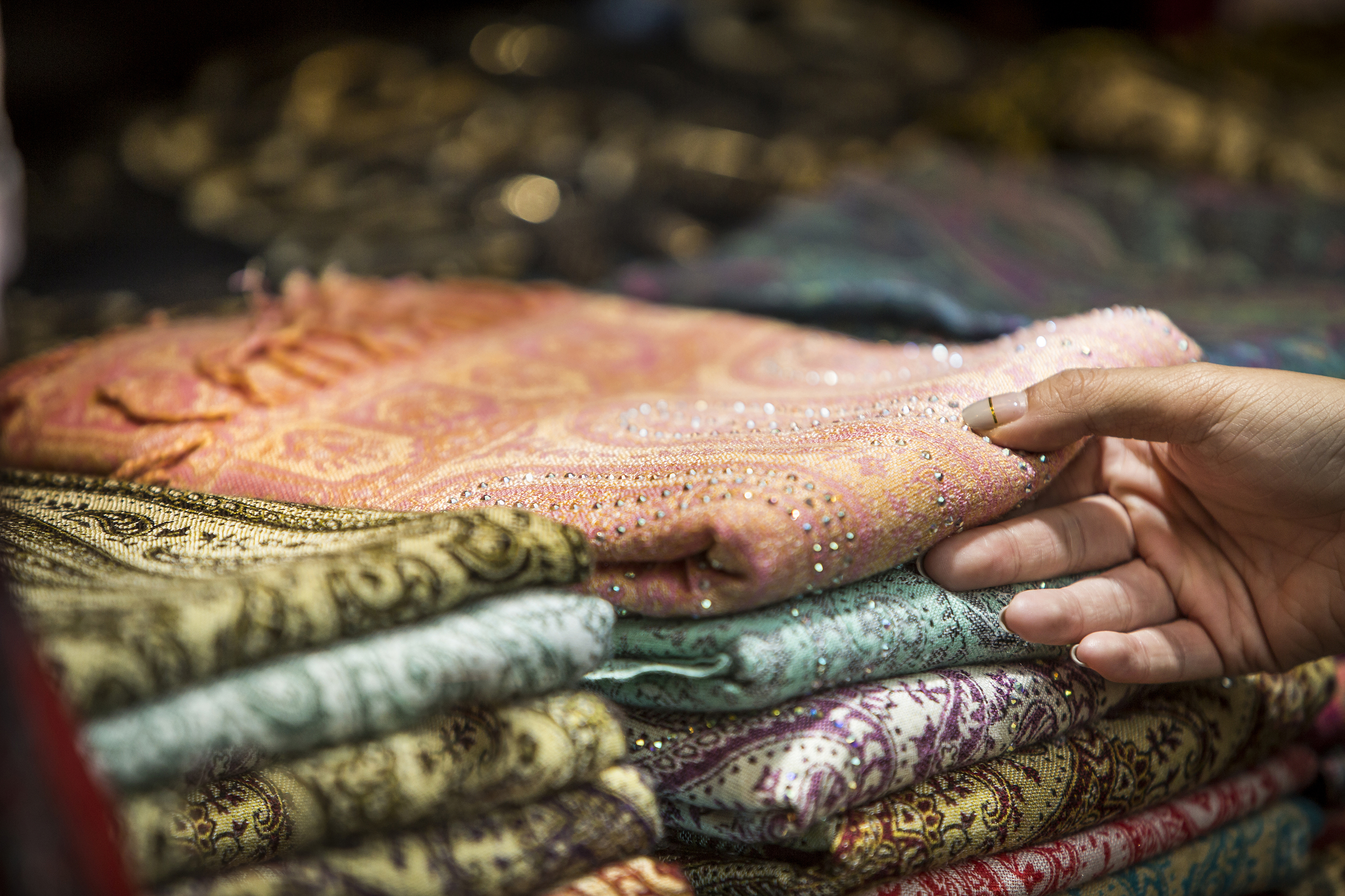 A female hand browsing patterned scarves at a market stall