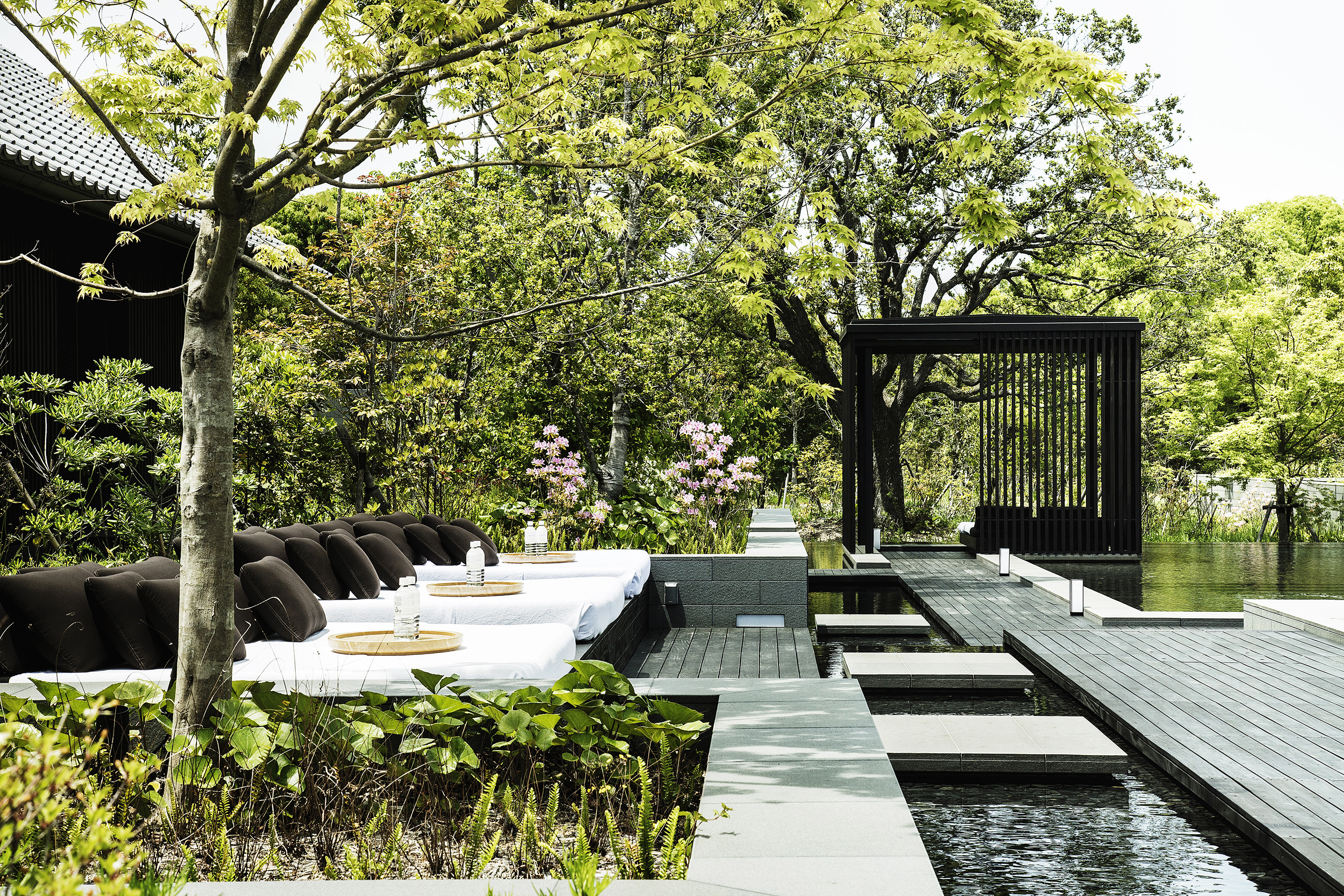 The outdoor pool of Amanemu surrounded by trees featuring wooden walkways leading to comfy loungers and a cabana