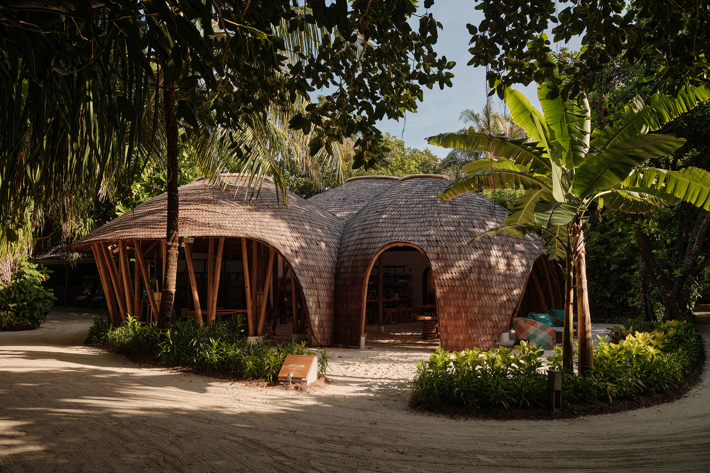 The thatched dome building of the Art Lab at Finolhu surrounded by sand and palms