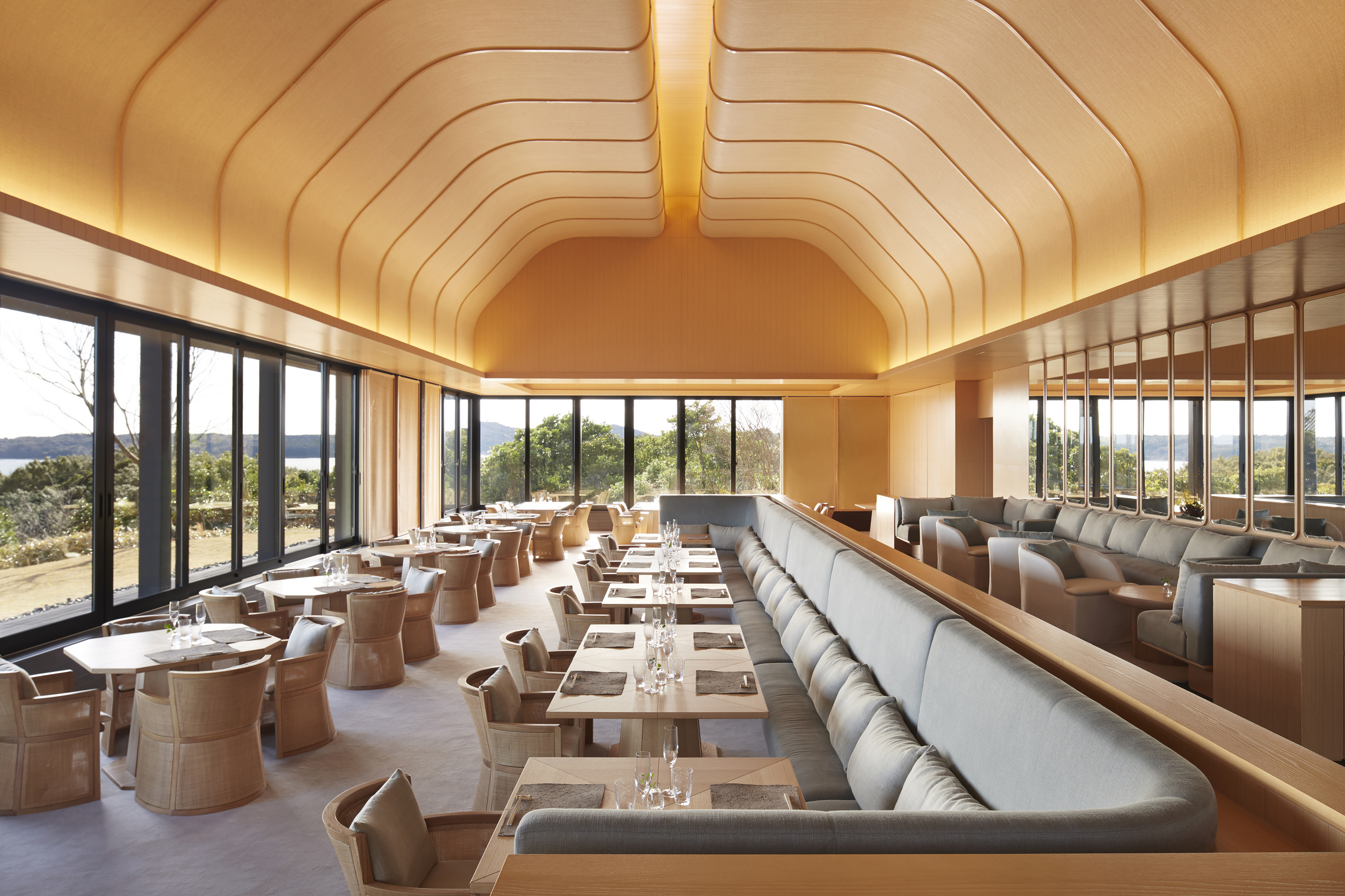 The stylish restaurant at Amanemu with sleek sofas and tables set for dinner beneath high arched ceilings with integrated lighting