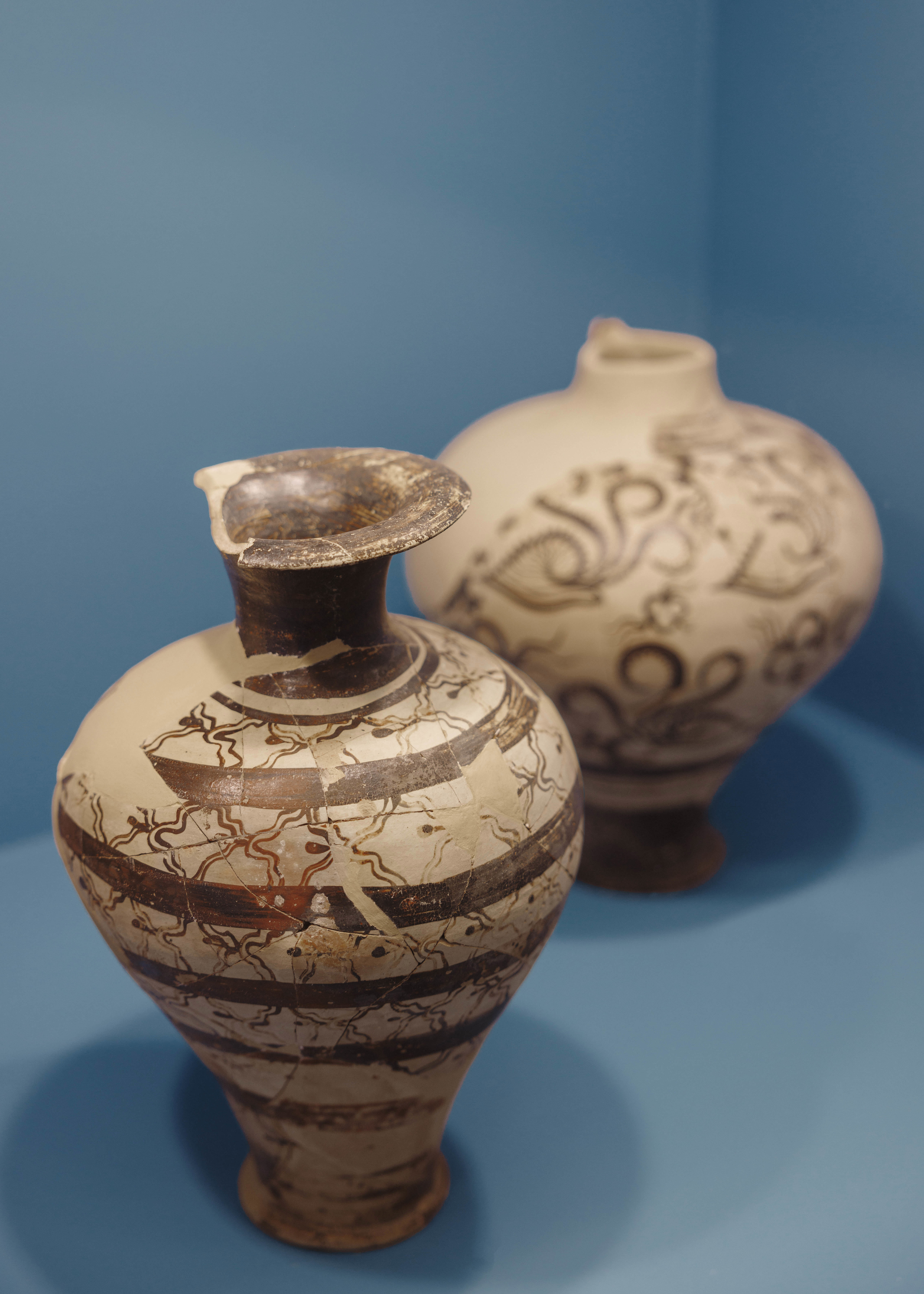 Ancient pots with brown artwork displayed in blue museum exhibition