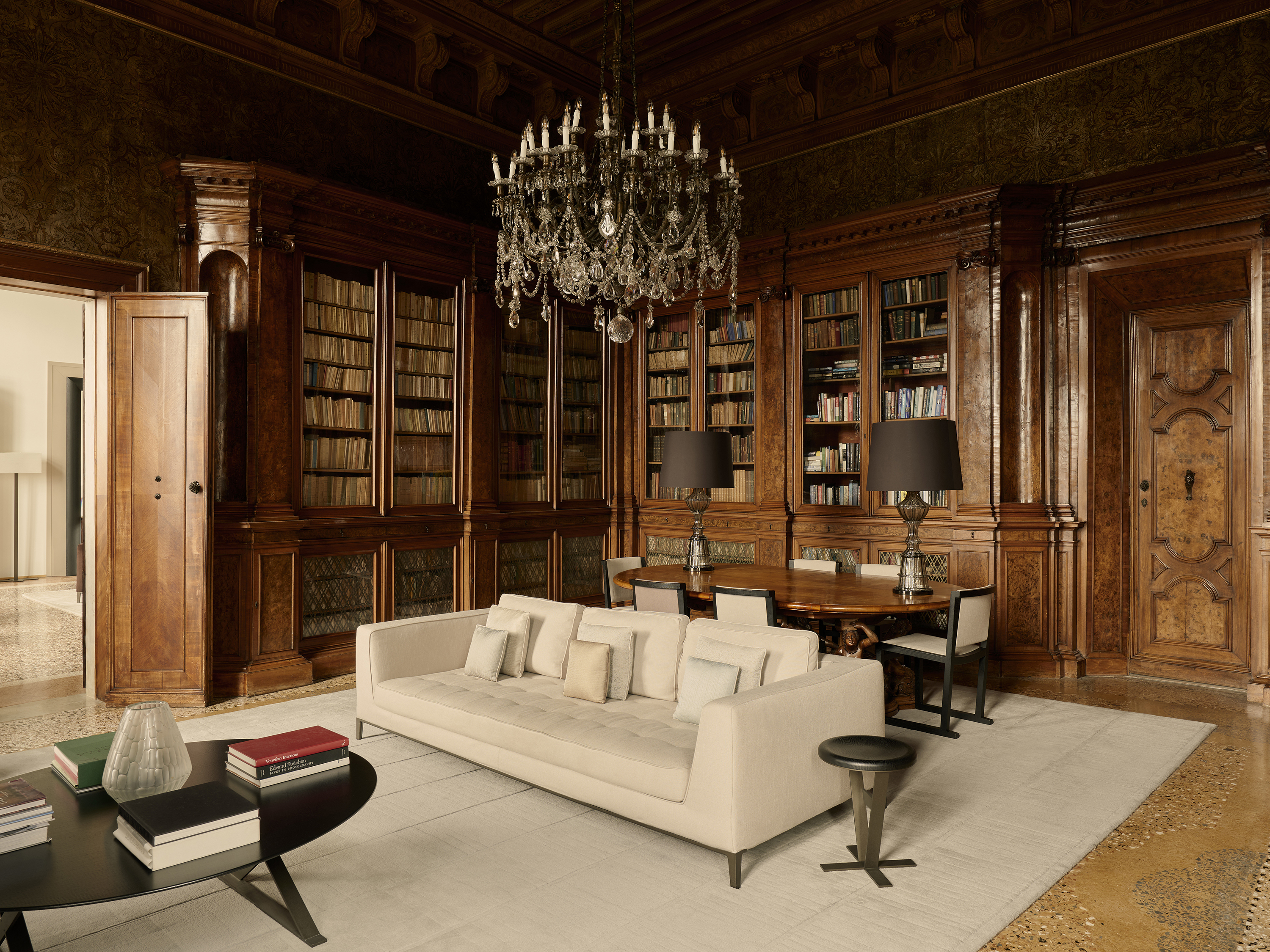 An ornate library room with large bookcases, a chandelier and comfy seating