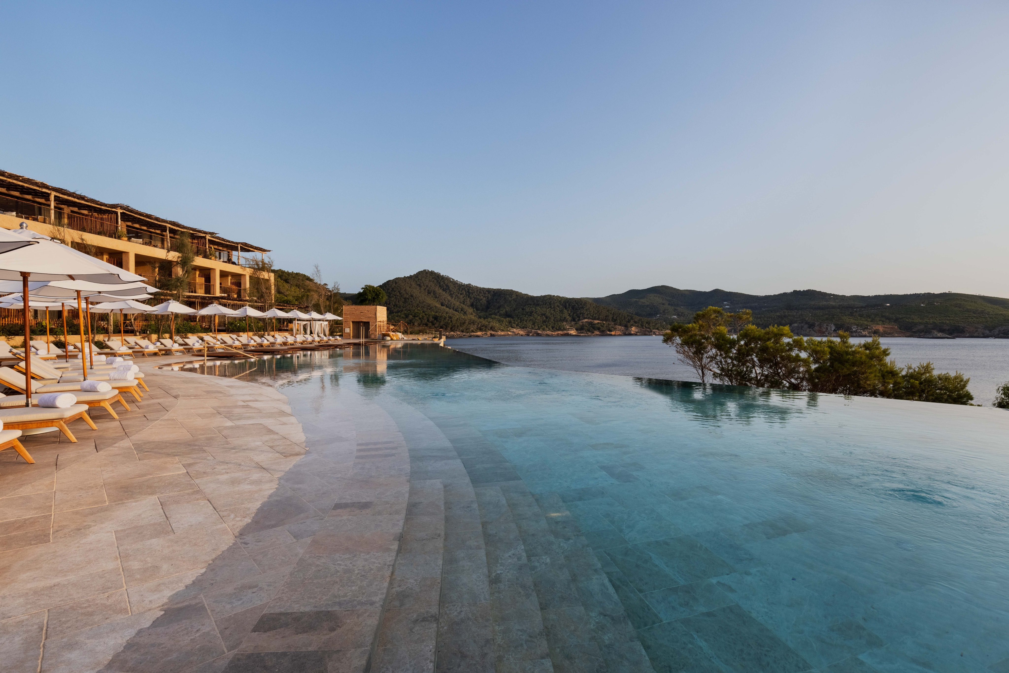 Luxurious infinity pool overlooking a serene lake and distant mountains at sunset.
