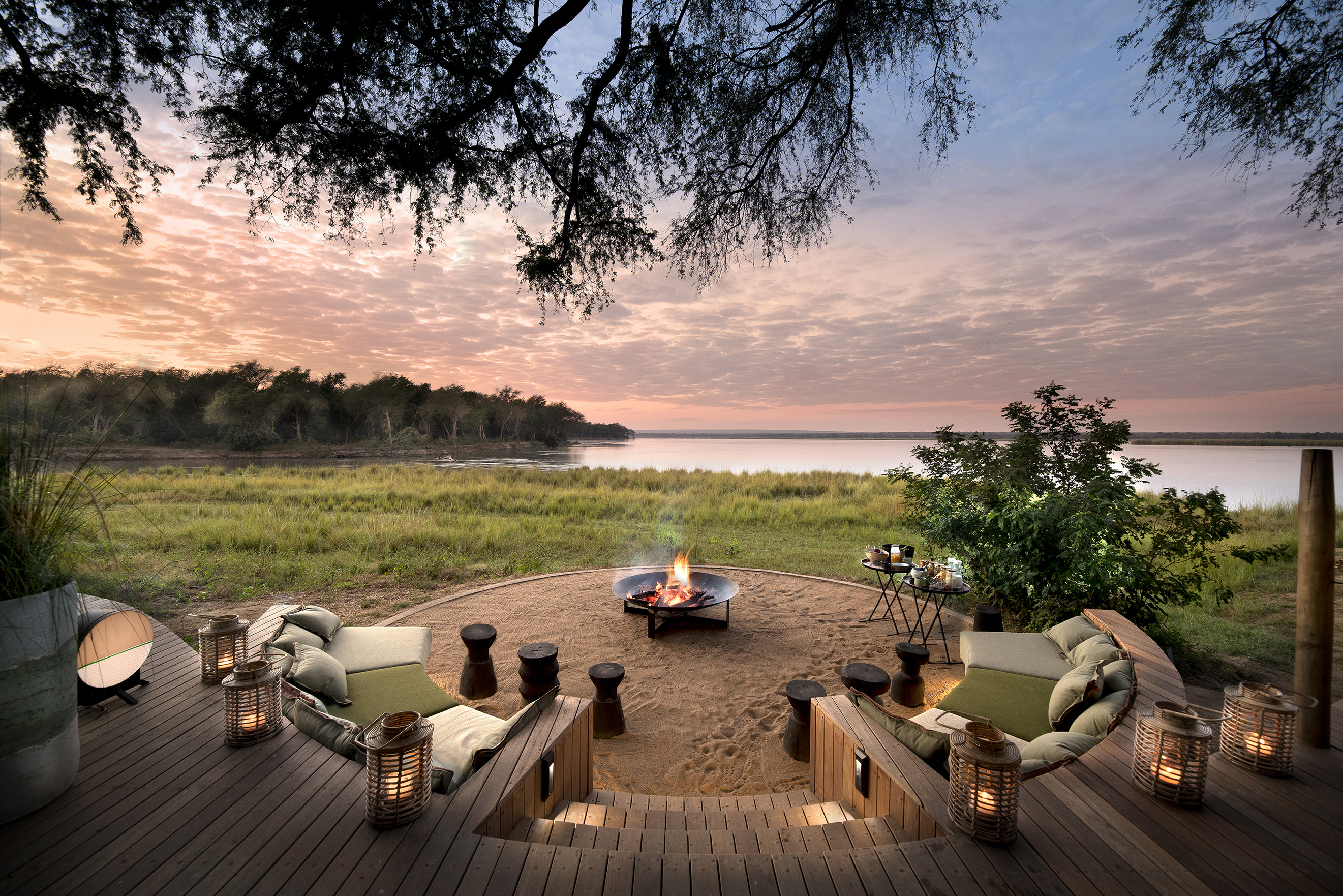 A circular firepit surrounded by comfy sofas and candles with a sweeping view of the Zambezi River and surrounding landscape