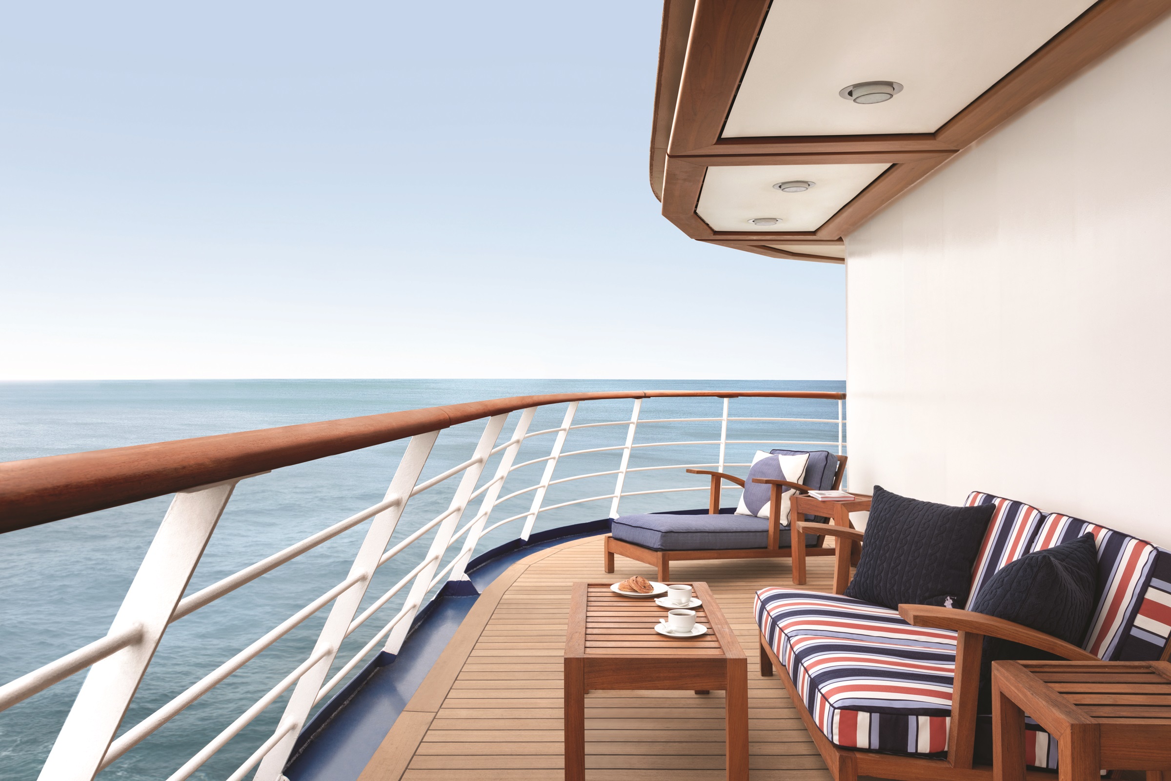 Private balcony on an Oceania Cruises ship with striped cushioned furniture, coffee table, and ocean view.